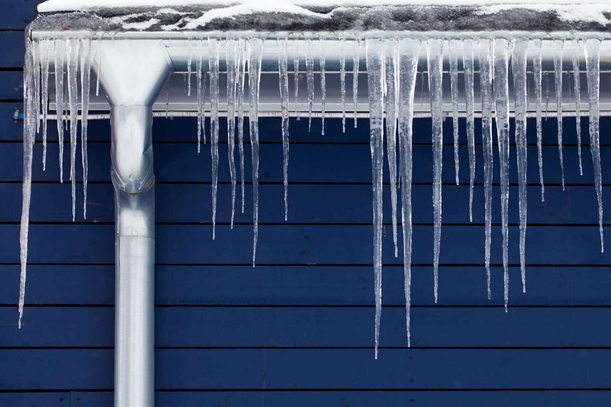 Icicles hang off a roof on a blue house