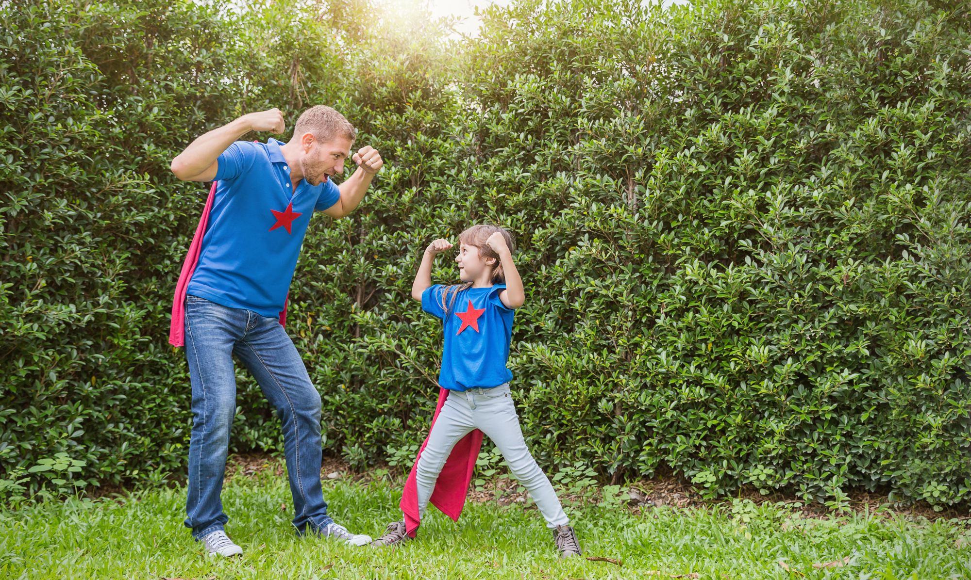 A father and his son pose as superheroes in the yard