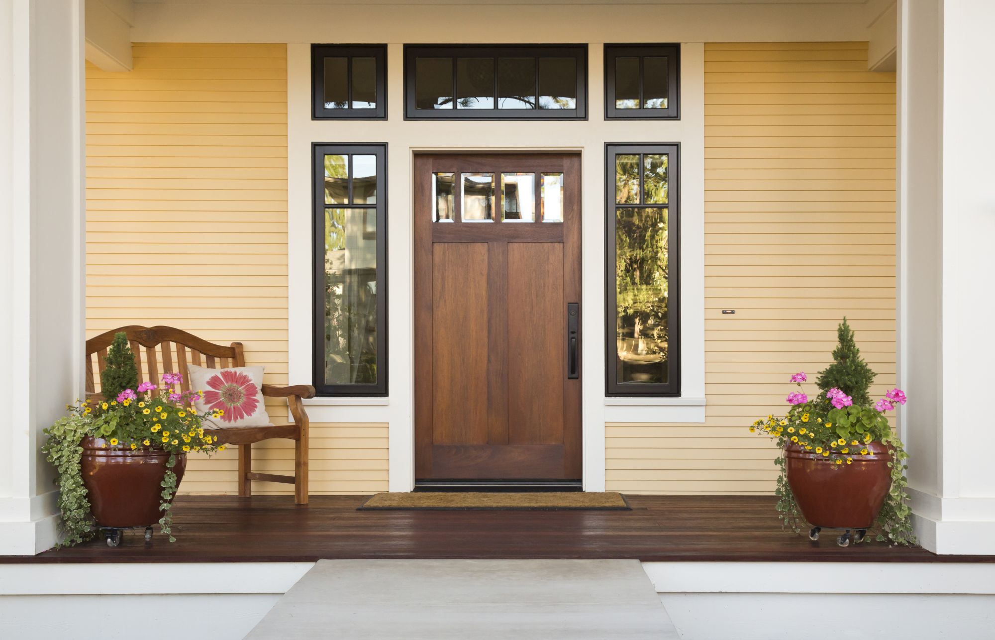 A wooden front door, with flowers and a bench nearby